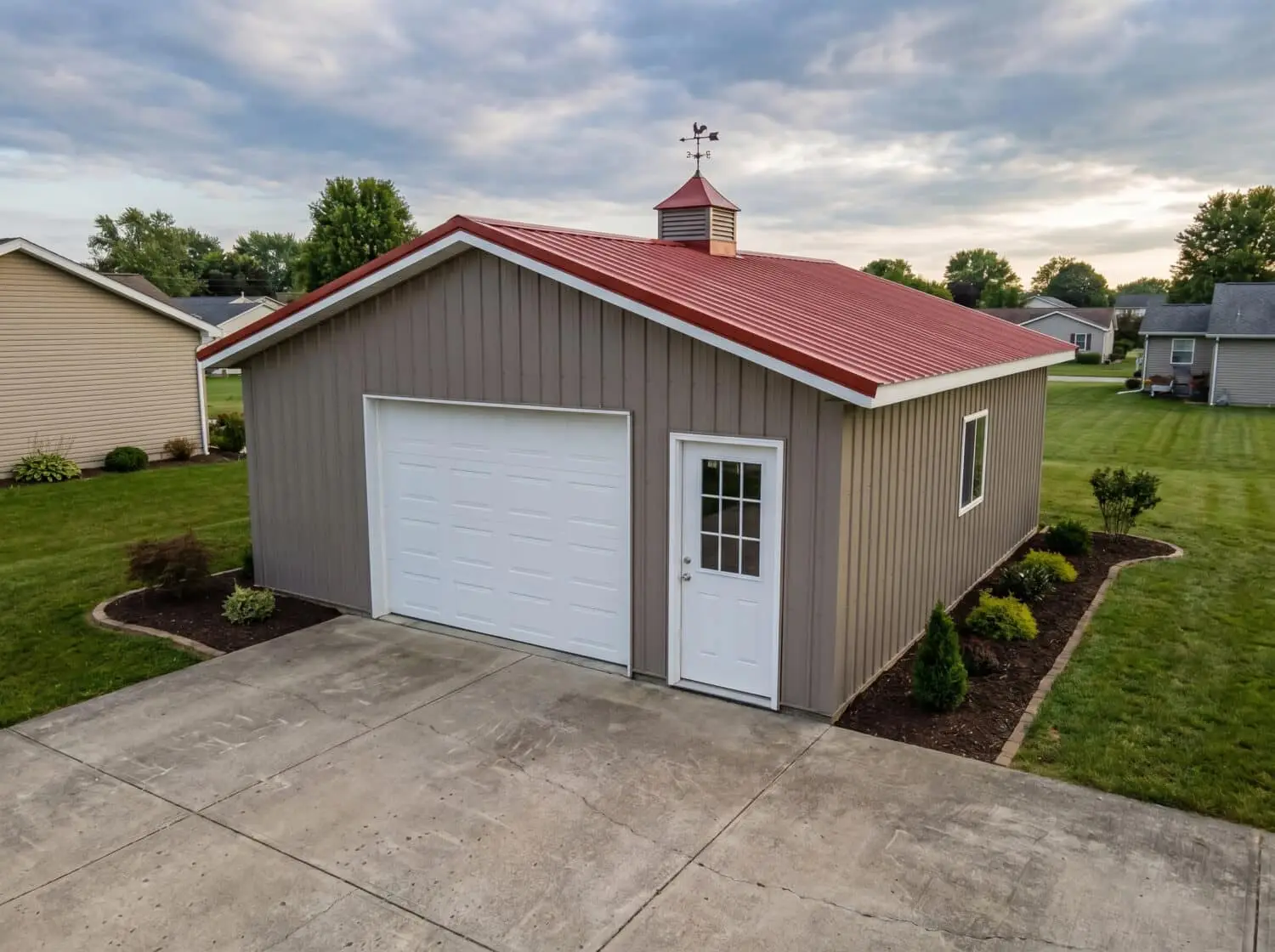 Simulated reference image of a metal garage or barn-style building with a red roof, white doors, and a concrete apron in a suburban setting.