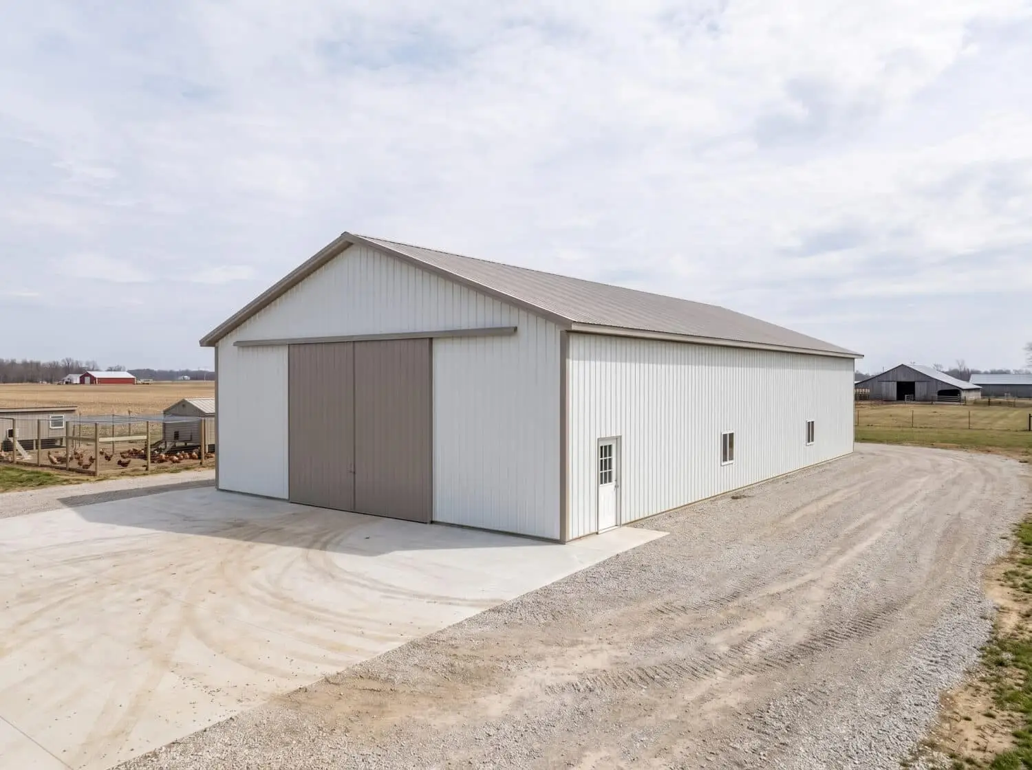A simulated image of a large white agricultural pole barn with a tan sliding front door and metal roof on a rural Columbus, Ohio property, shown from the front-left corner with concrete apron and gravel driveway.