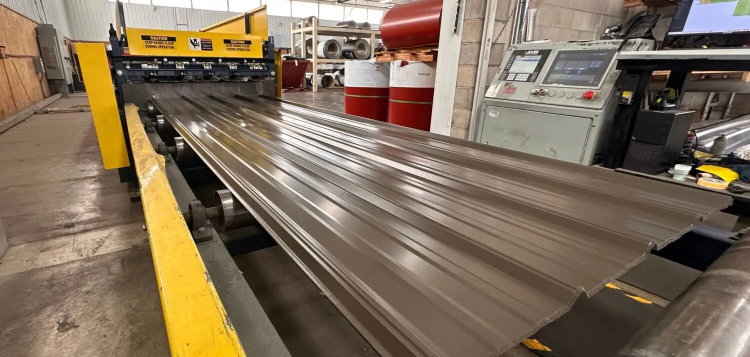 Metal roofing panel being roll formed on site inside a production facility